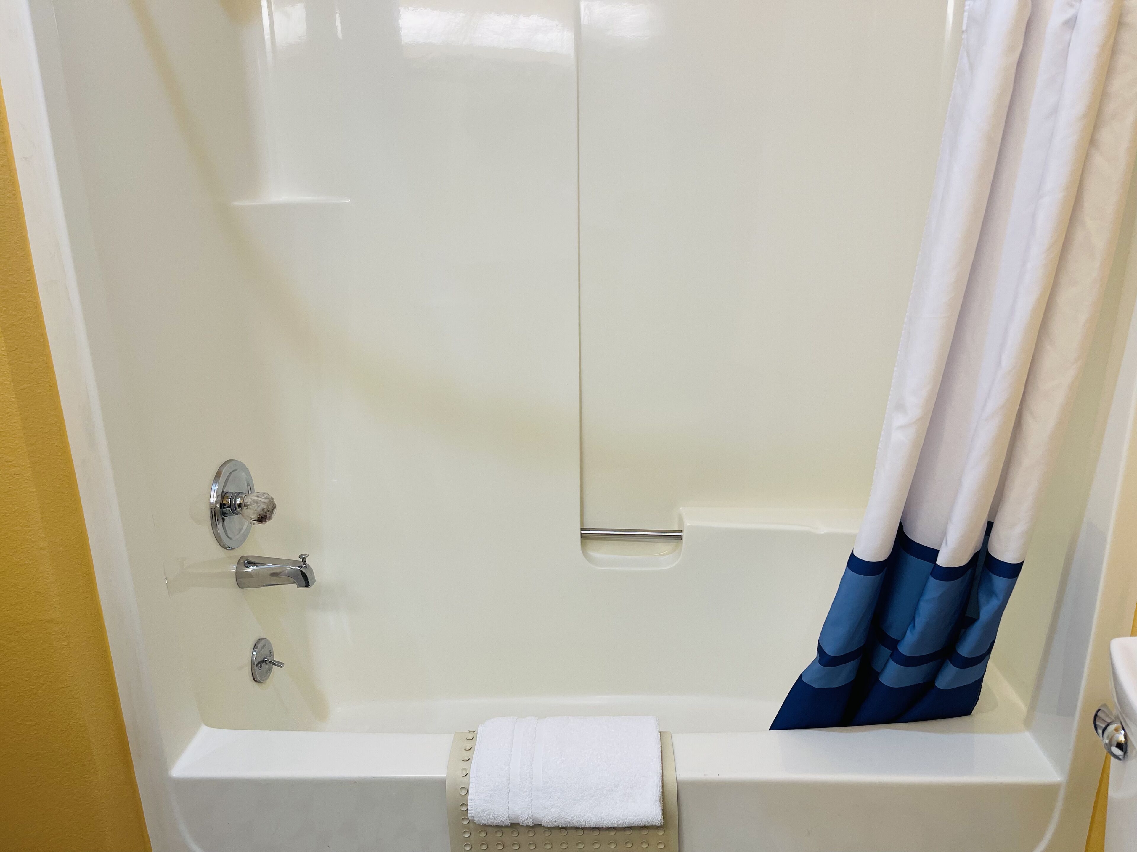 Una bañera con cortina blanca, una toalla y un grifo.