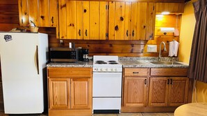 A kitchen with wooden cabinets, a white refrigerator, a microwave, a stove, and a sink.