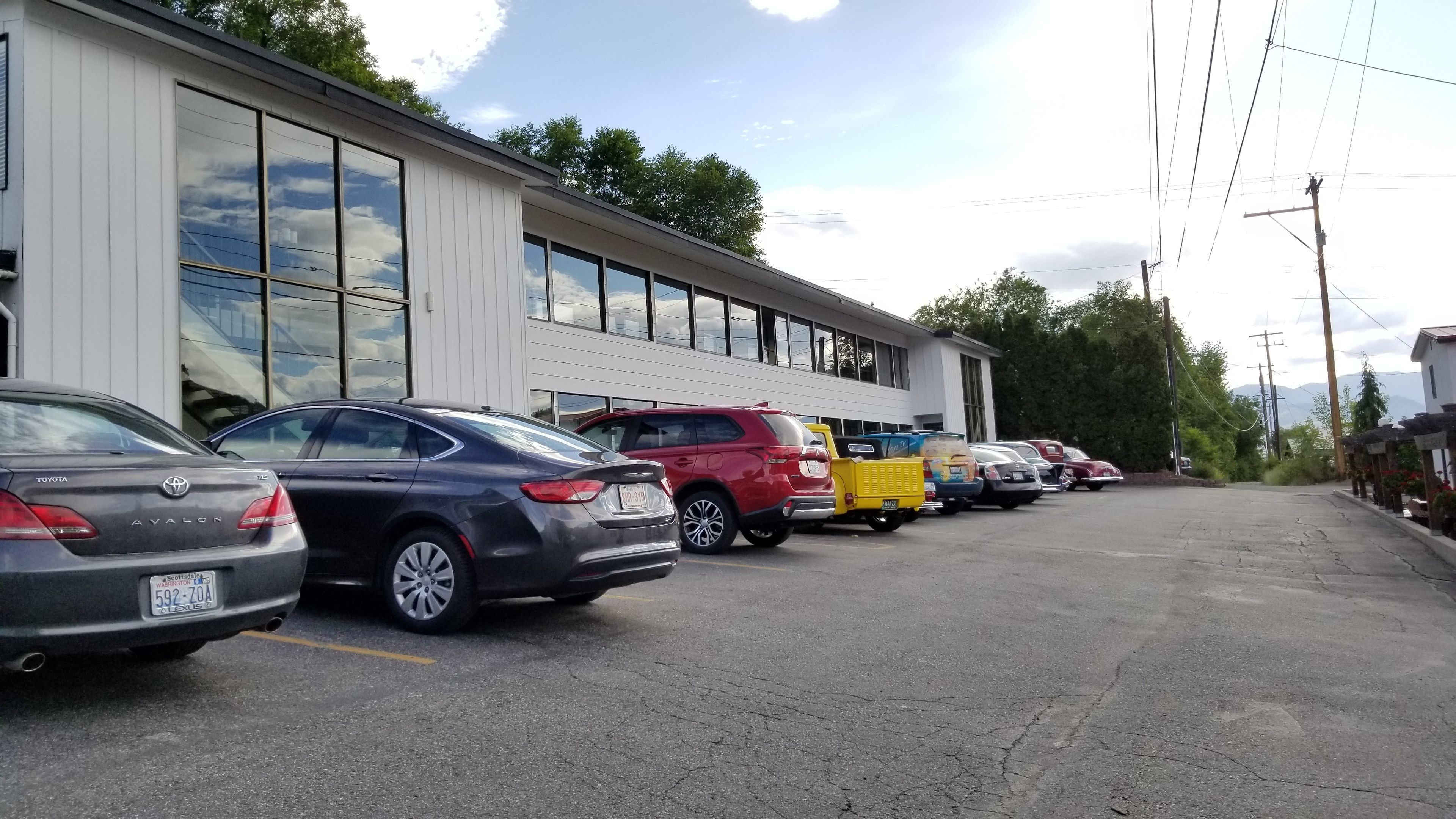 A parking lot with several cars parked in front of a building with large windows.