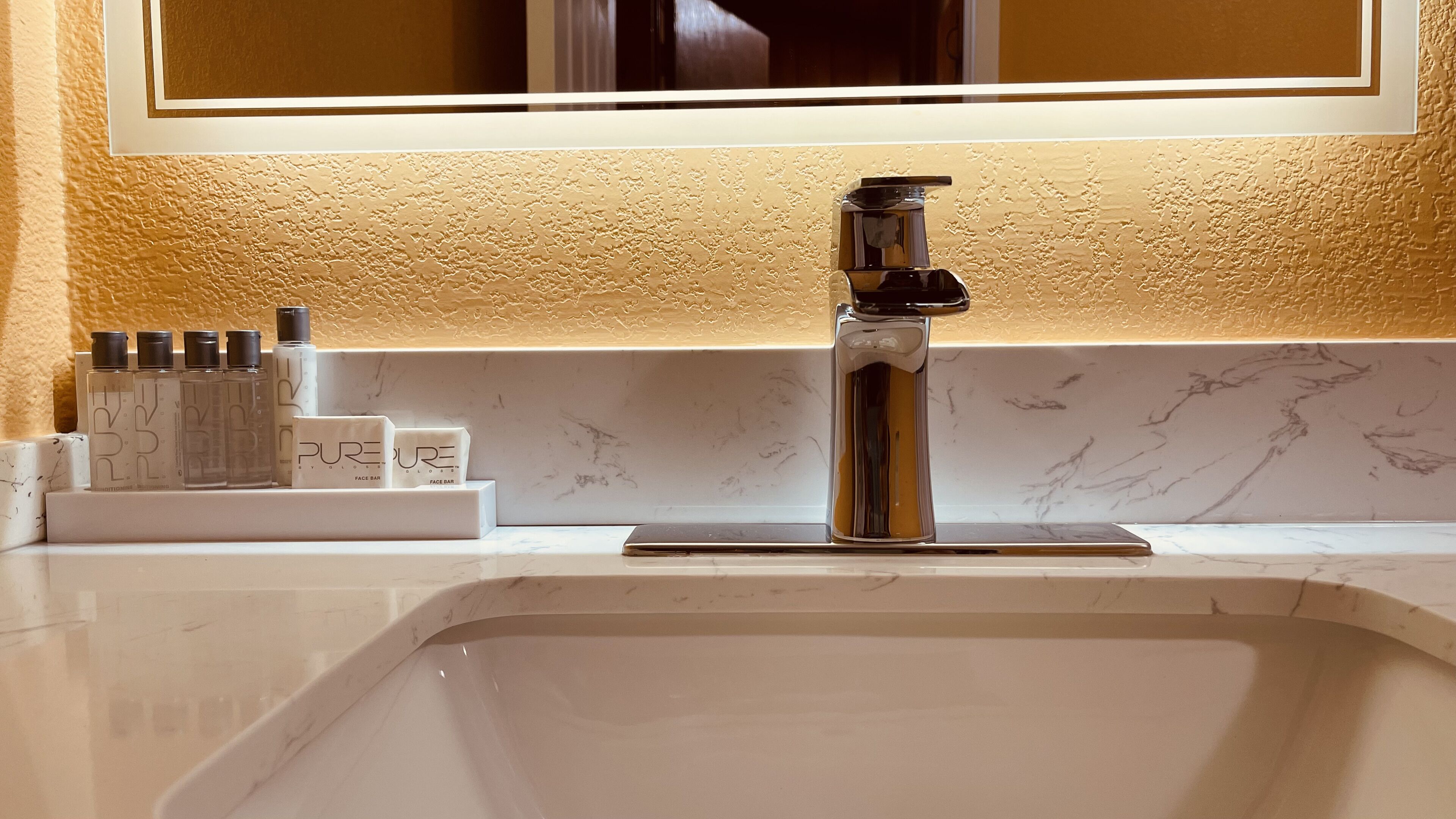 Un lavamanos de baño con un grifo moderno, un espejo encima y un juego de artículos de aseo en la encimera.