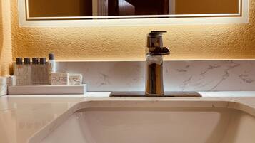 Un lavamanos de baño con un grifo moderno, un espejo encima y un juego de artículos de aseo en la encimera.