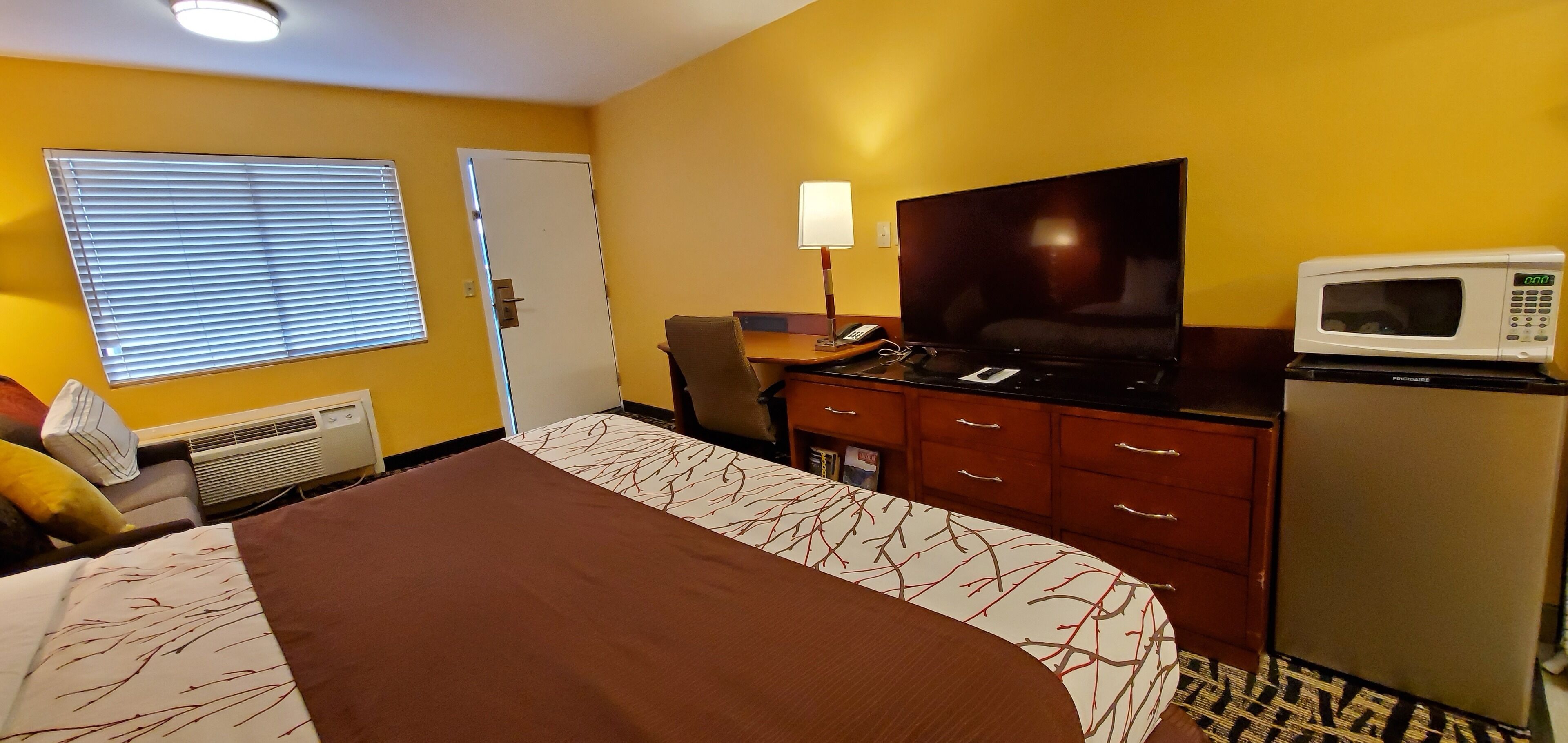 Una habitación de hotel con cama, escritorio, televisor de pantalla plana, microondas y refrigerador.