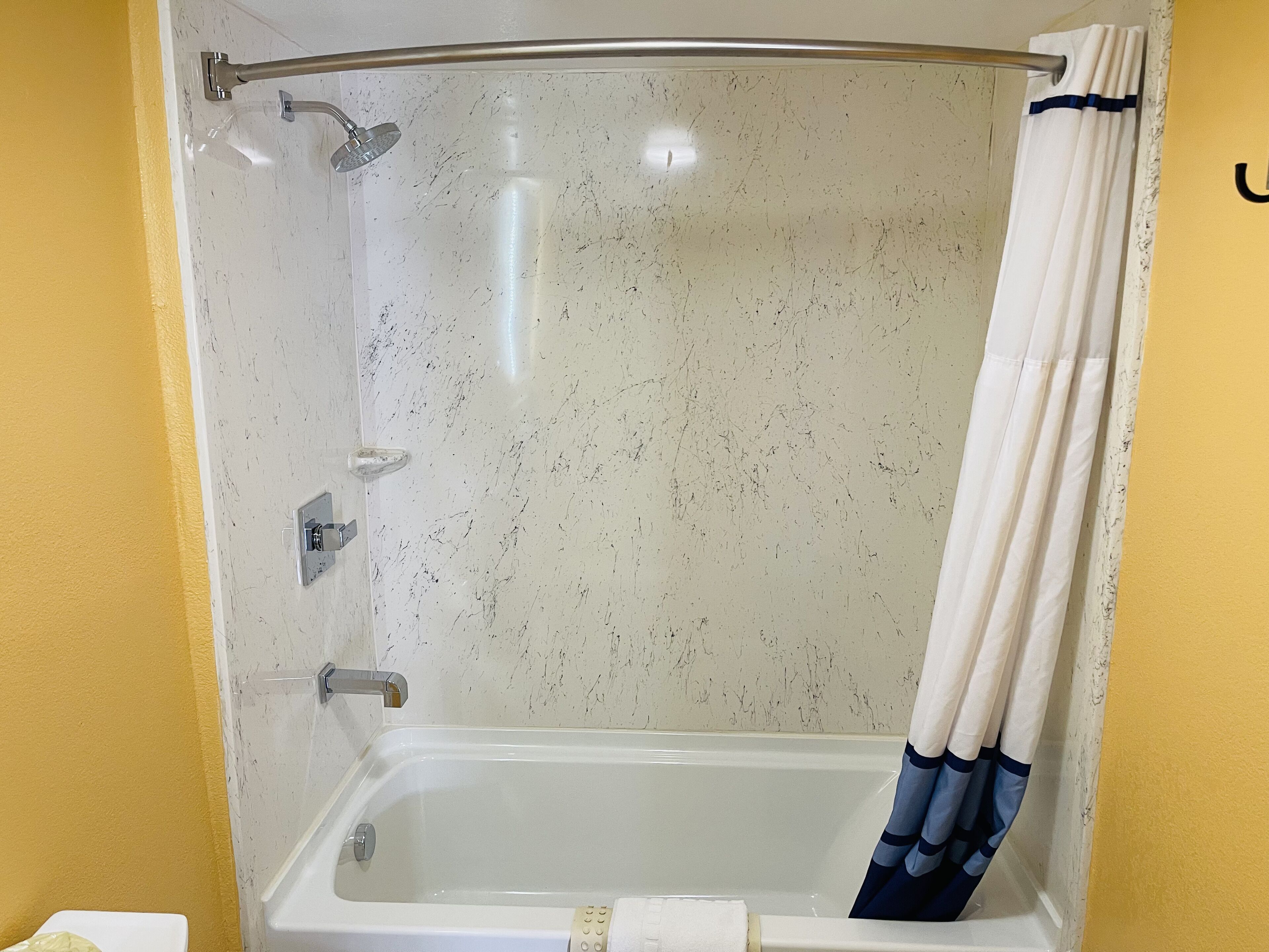 Une salle de bain avec une douche, une baignoire blanche et un mur jaune.