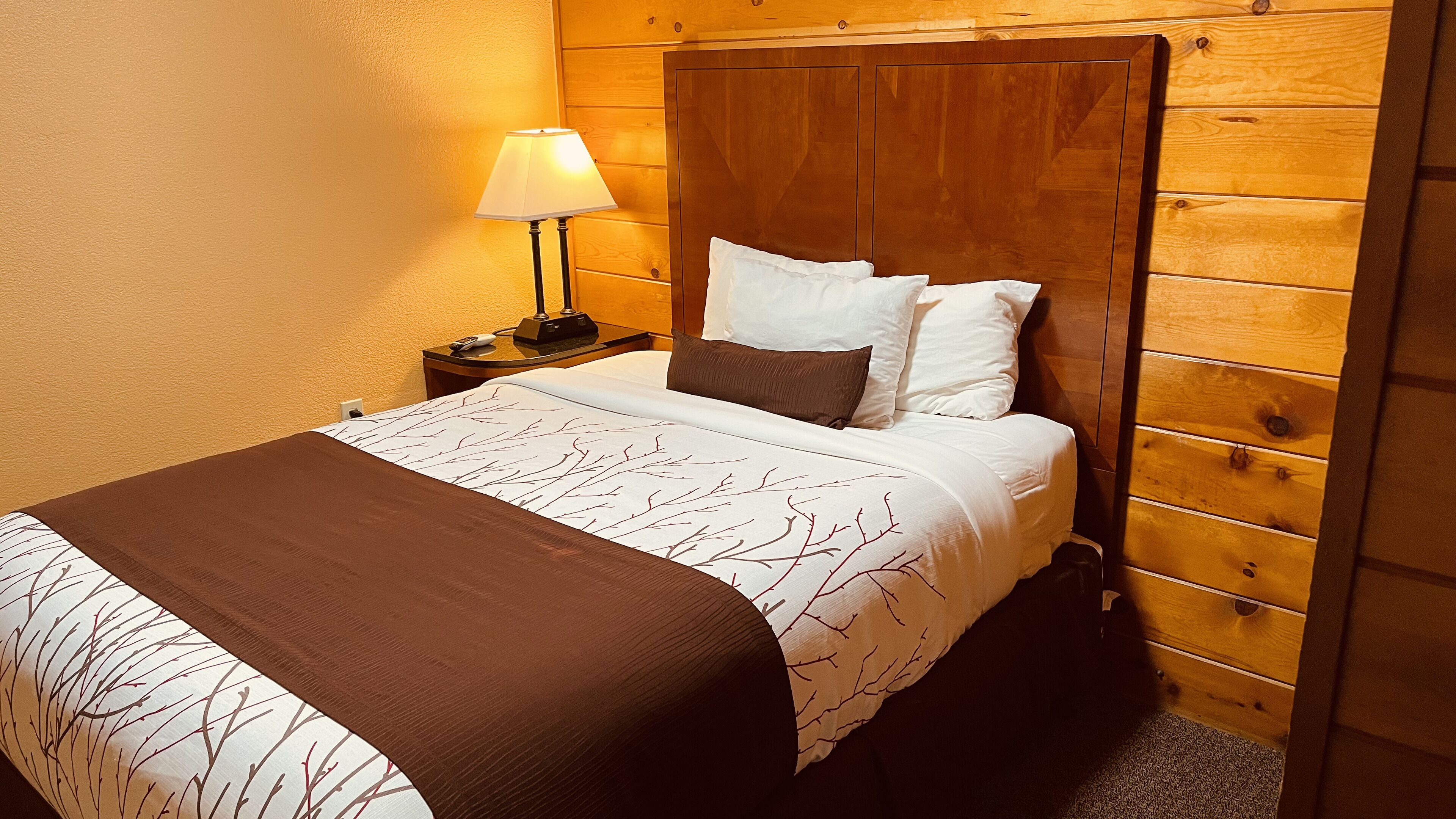A neatly made bed with a patterned bedspread, a bedside lamp, and a wooden headboard.