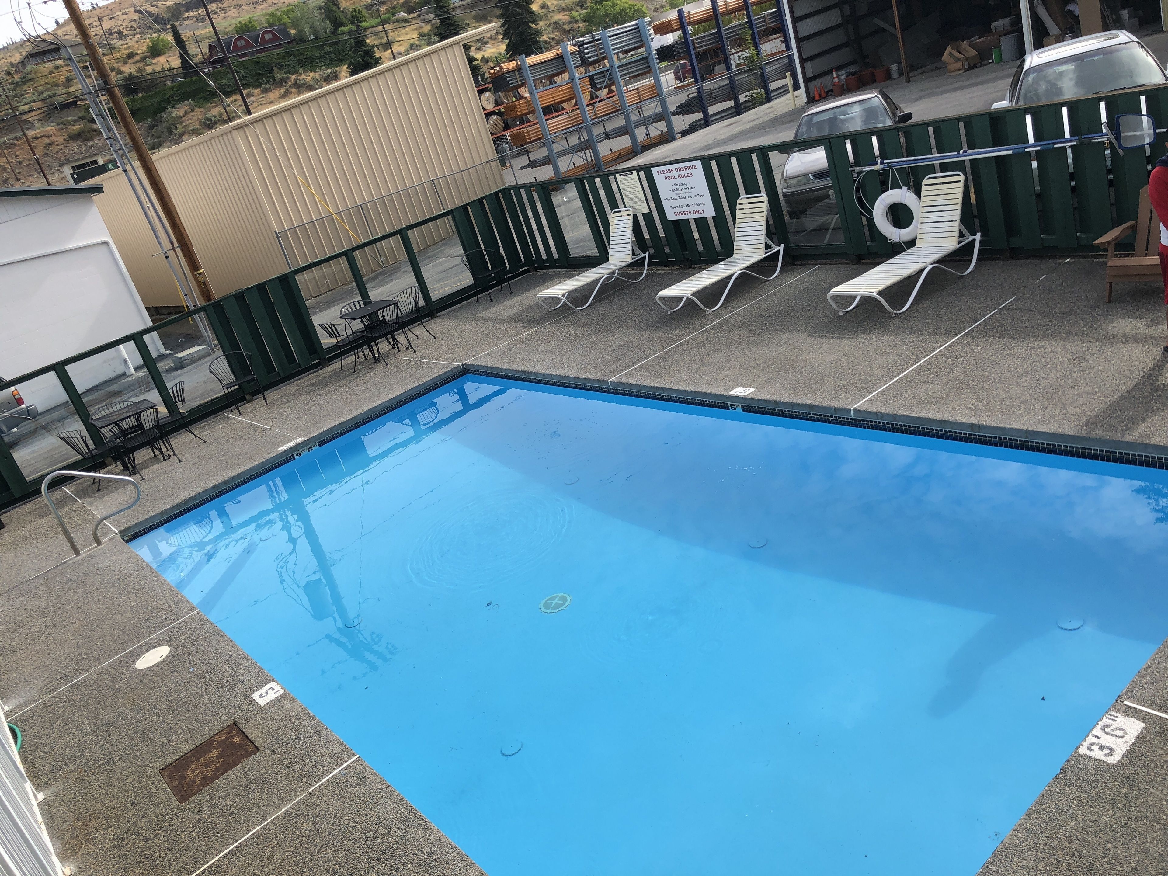 Piscina en la azotea con superficie de agua azul cristalina, rodeada por una barandilla metálica y varias sillas reclinables blancas.