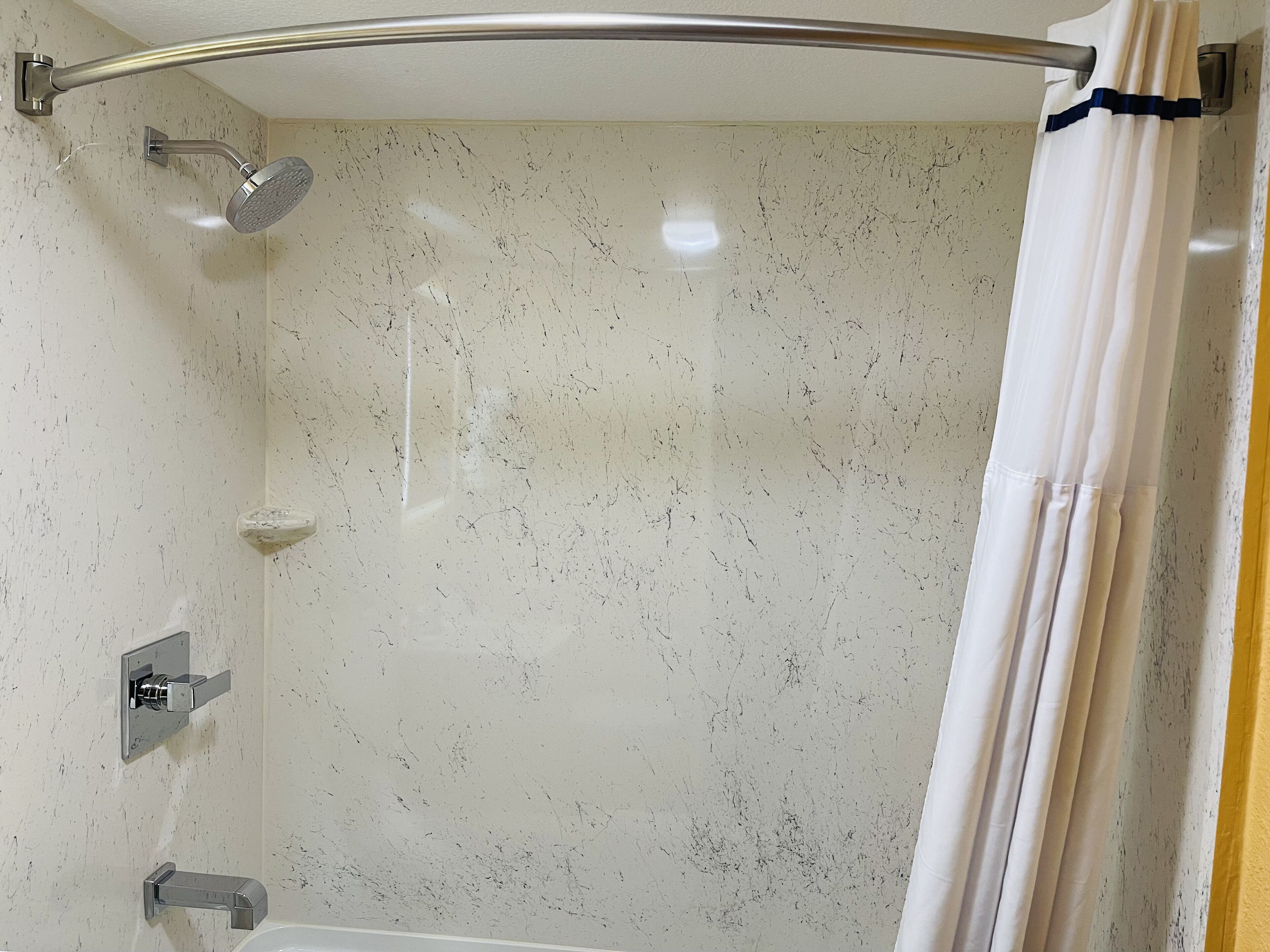 Une douche avec une porte en verre, un pommeau de douche à main et un robinet mural.