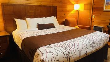 A wooden-paneled room with a bed, a nightstand, a lamp, and a framed picture on the wall.