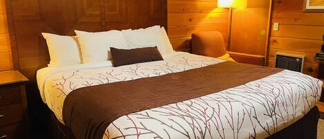 A wooden-paneled room with a bed, a nightstand, a lamp, and a framed picture on the wall.