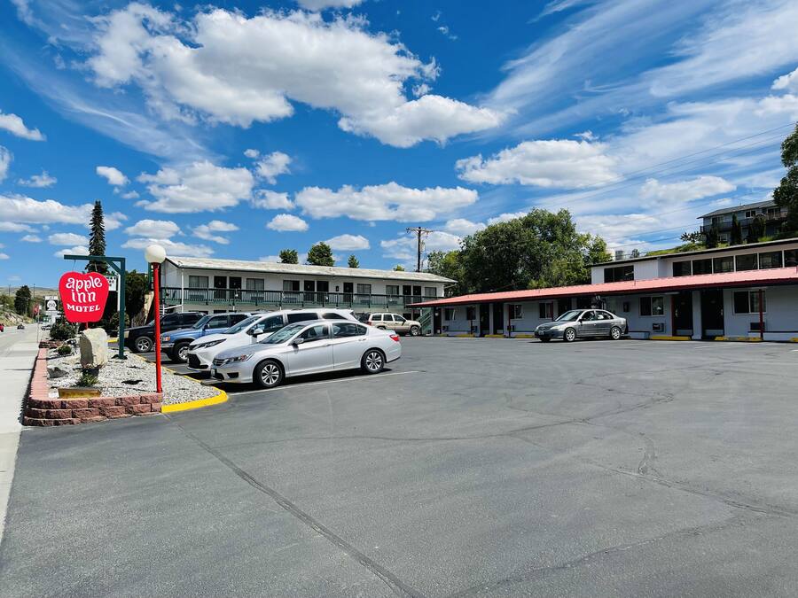 A motel with a red and white sign, a parking lot with several cars, and a building with a red roof.