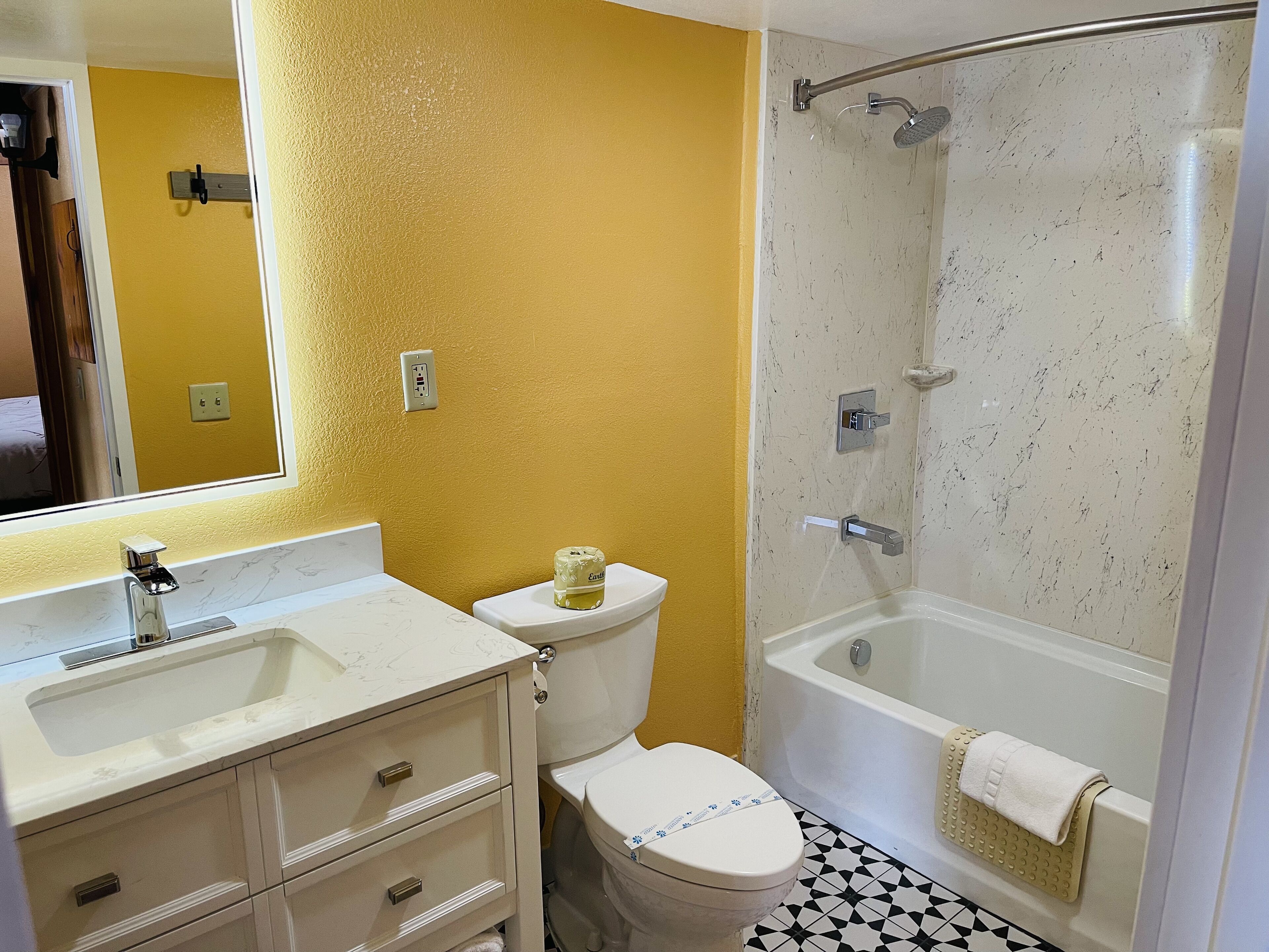 A bathroom with a yellow wall, a white sink, a toilet, and a bathtub with a shower head.