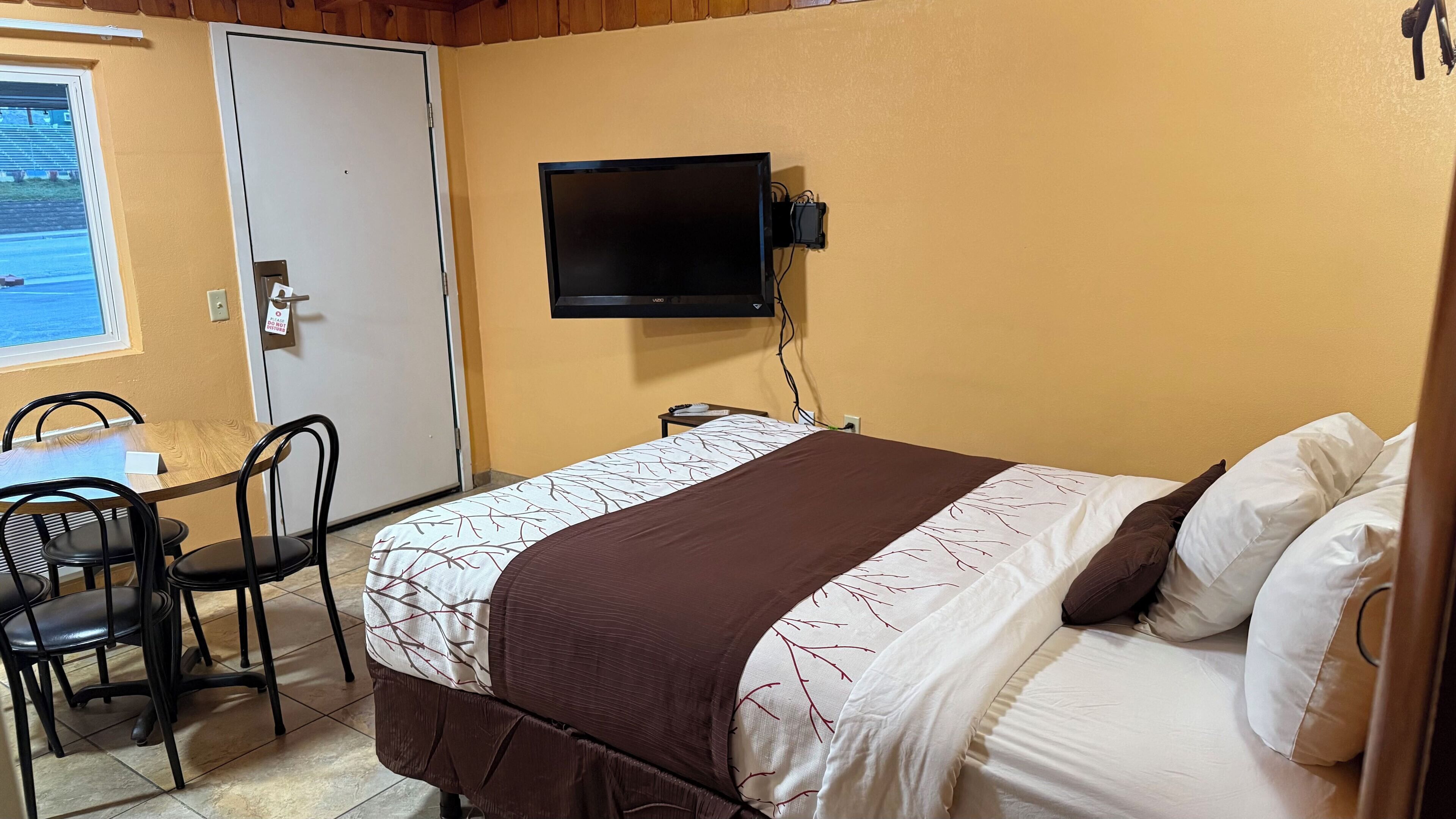 A hotel room with a bed, a desk, and a television mounted on the wall.