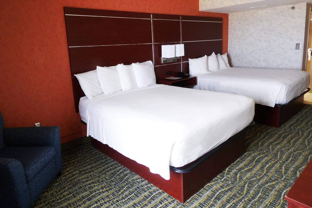 Ein Hotelzimmer mit zwei Betten, einem Nachttisch, einem Sessel und einem gemusterten Teppich.