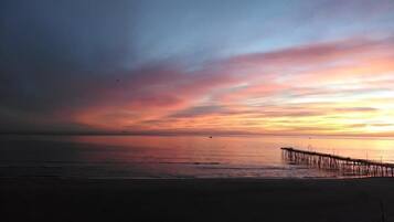 A beach with a pier extending into calm waters during sunset.