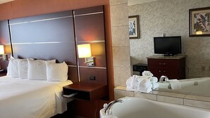 A hotel room with a large bed, a sitting area, a television, a bathtub, and a bathroom with a sink and mirror. - Breakers Resort Inn (Virginia Beach)