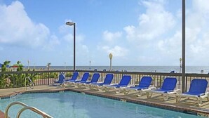A pool area with blue lounge chairs and a view of the ocean. - Breakers Resort Inn (Virginia Beach)