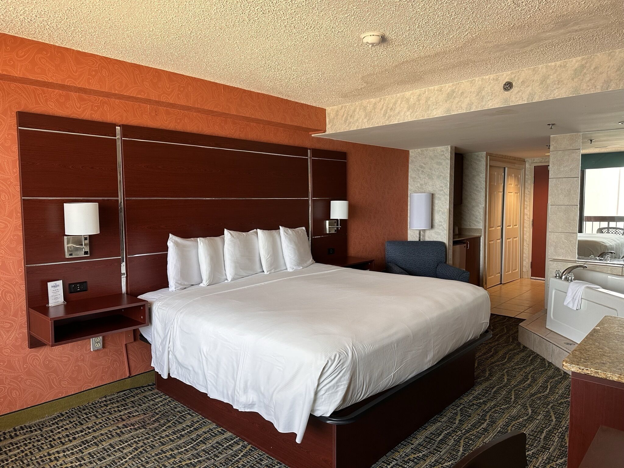 Een hotelkamer met een groot bed, een bureau, een stoel, een badkamer met bad en een spiegel.
