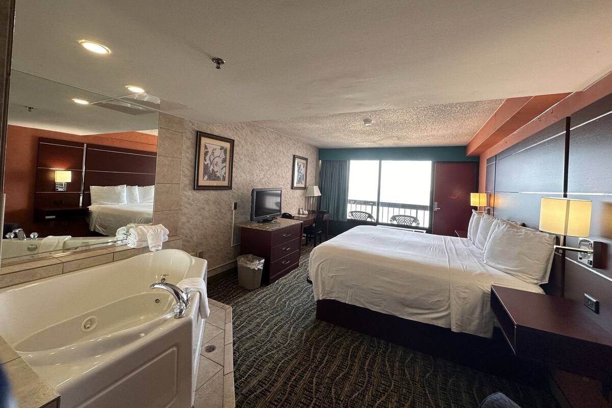 Ein Hotelzimmer mit einem großen Bett, einem separaten Badezimmer mit Badewanne, einem Fernseher und einem großen Fenster mit Blick.