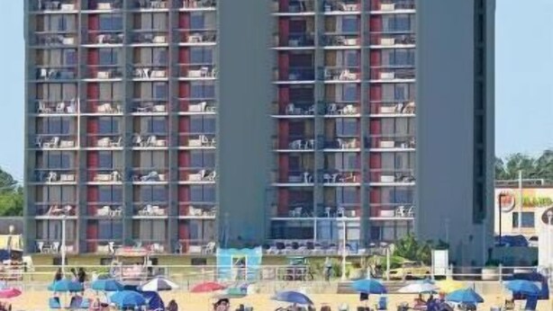 A multi-story hotel with balconies, located near a beach with umbrellas and people. - Breakers Resort Inn (Virginia Beach)