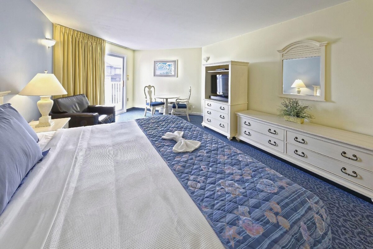 A hotel room with a bed, a desk, a chair, a dresser, and a television.
