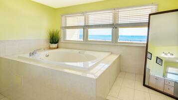 A bathroom with a large bathtub, a potted plant, and a view of the beach through the window.