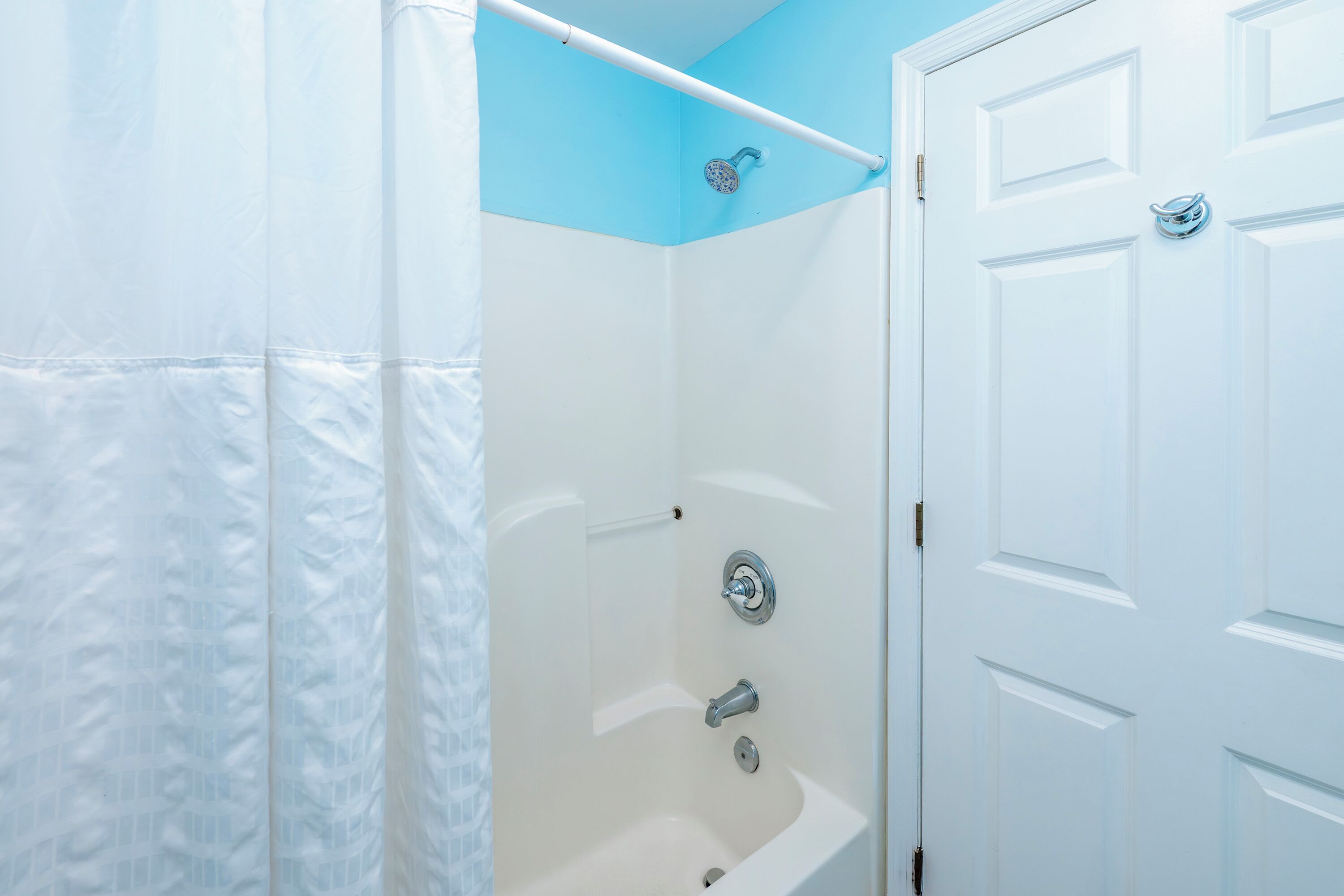 Un baño con una bañera blanca, ducha y una puerta con pomo.