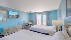 Habitación de hotel con dos camas, un escritorio, una silla, un aparador y un balcón con vistas.