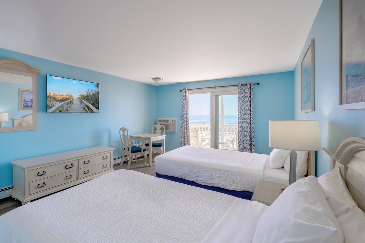 A hotel room with two beds, a desk, a chair, a dresser, and a balcony with a view.