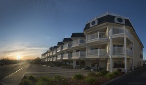 Un hotel de varios pisos con balcones, un estacionamiento y vistas al atardecer.