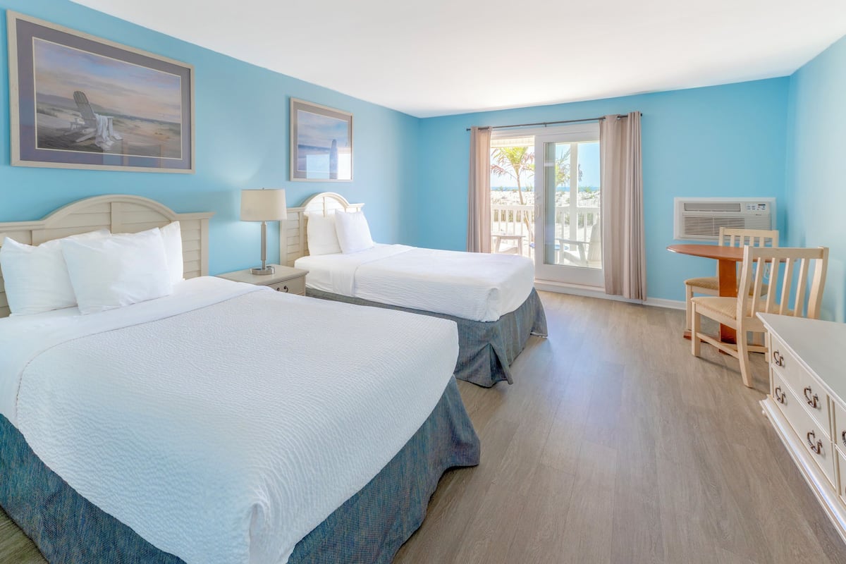 A hotel room with two beds, a desk, a chair, and a TV.