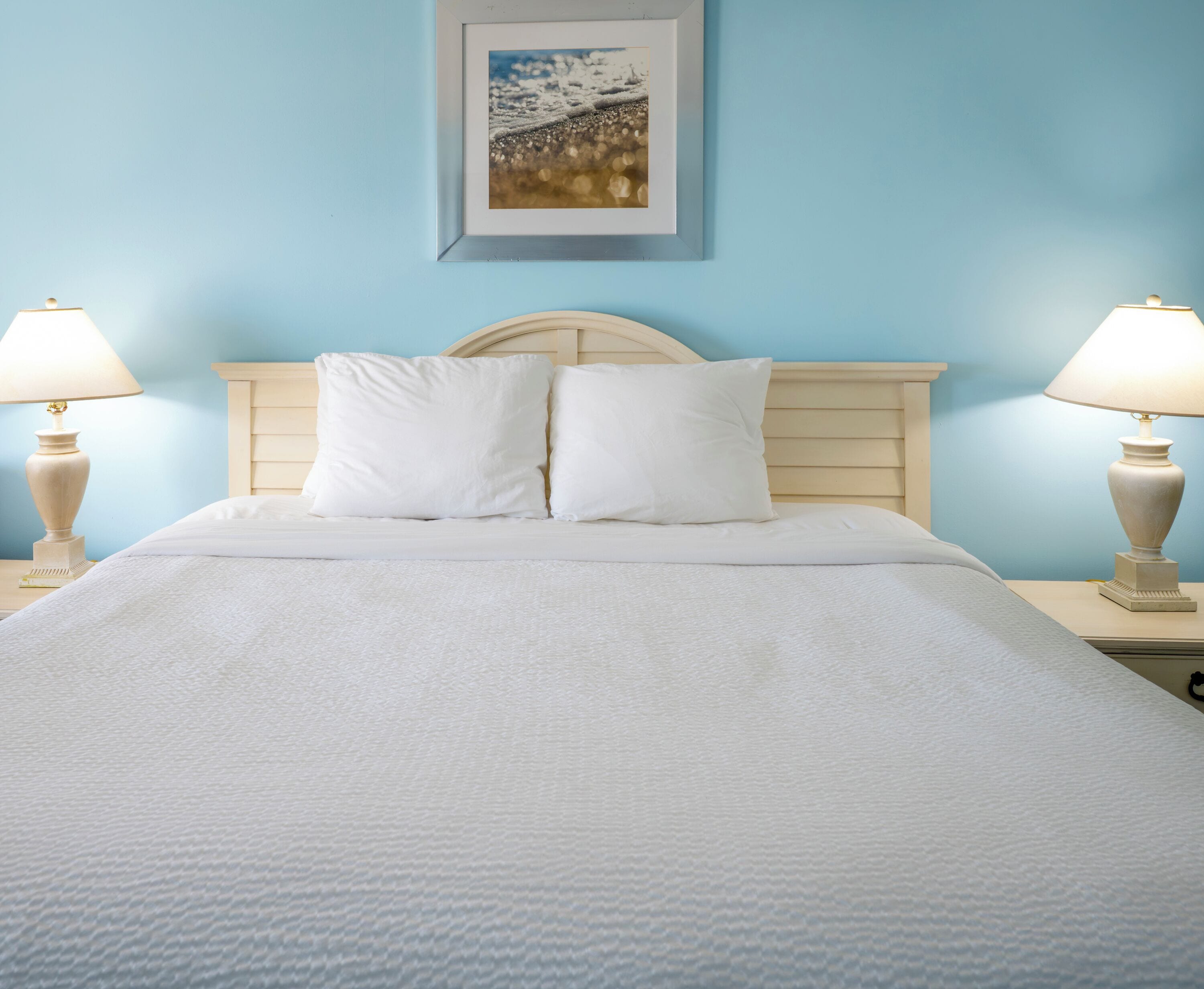 Ein ordentlich gemachtes Bett mit weißer Bettwäsche, einem Holzkopfschild und zwei Nachttischlampen auf beiden Seiten.