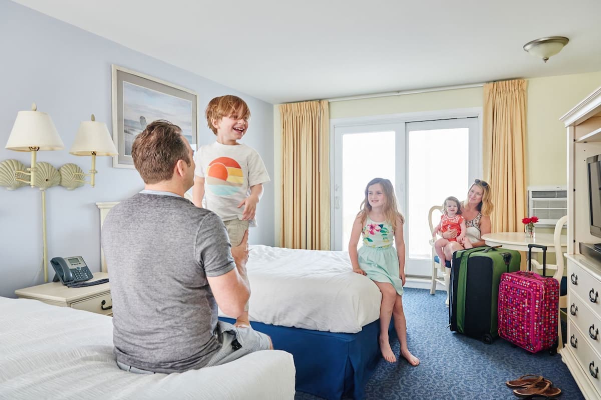 A hotel room with a bed, a desk with a phone, a TV, and a window with curtains.