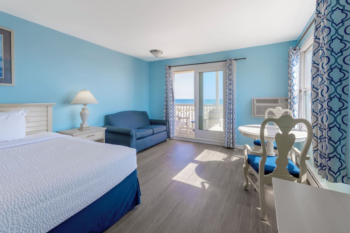 A hotel room with a bed, a sofa, a dining table with chairs, and a balcony with a view.