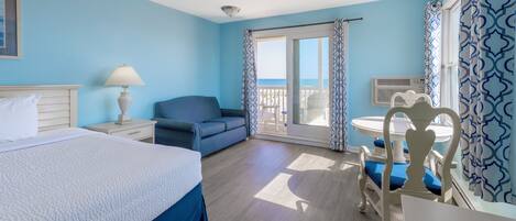 A hotel room with a bed, a sofa, a dining table with chairs, and a balcony with a view.