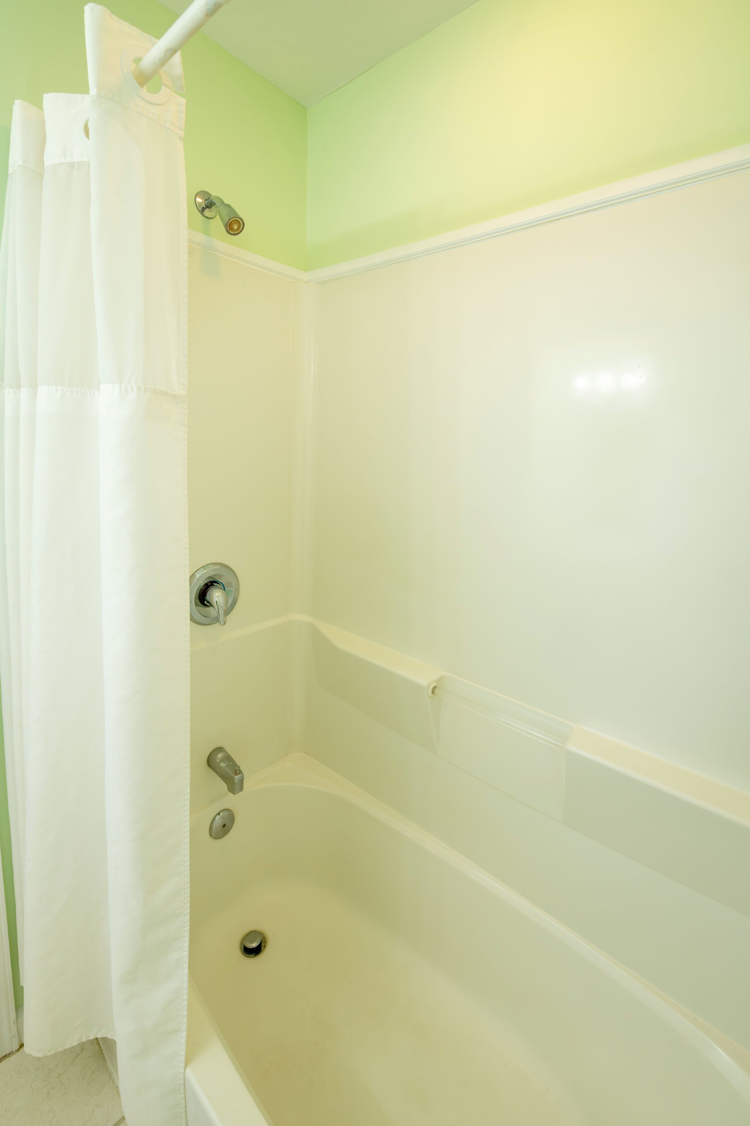 A bathroom with a bathtub, shower curtain, and a wall-mounted faucet.