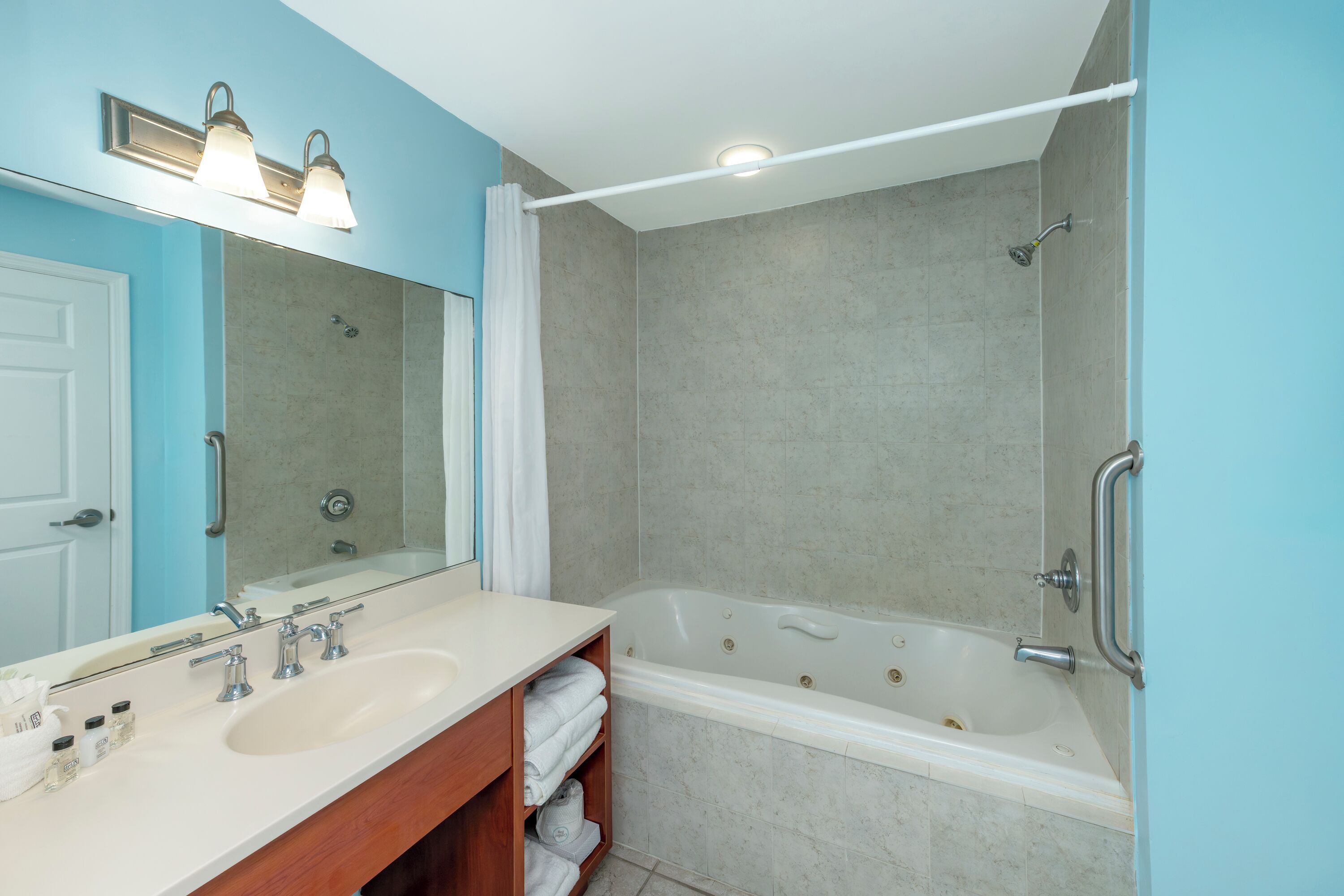 A bathroom with a double sink vanity, a large mirror, a bathtub, and a shower area.