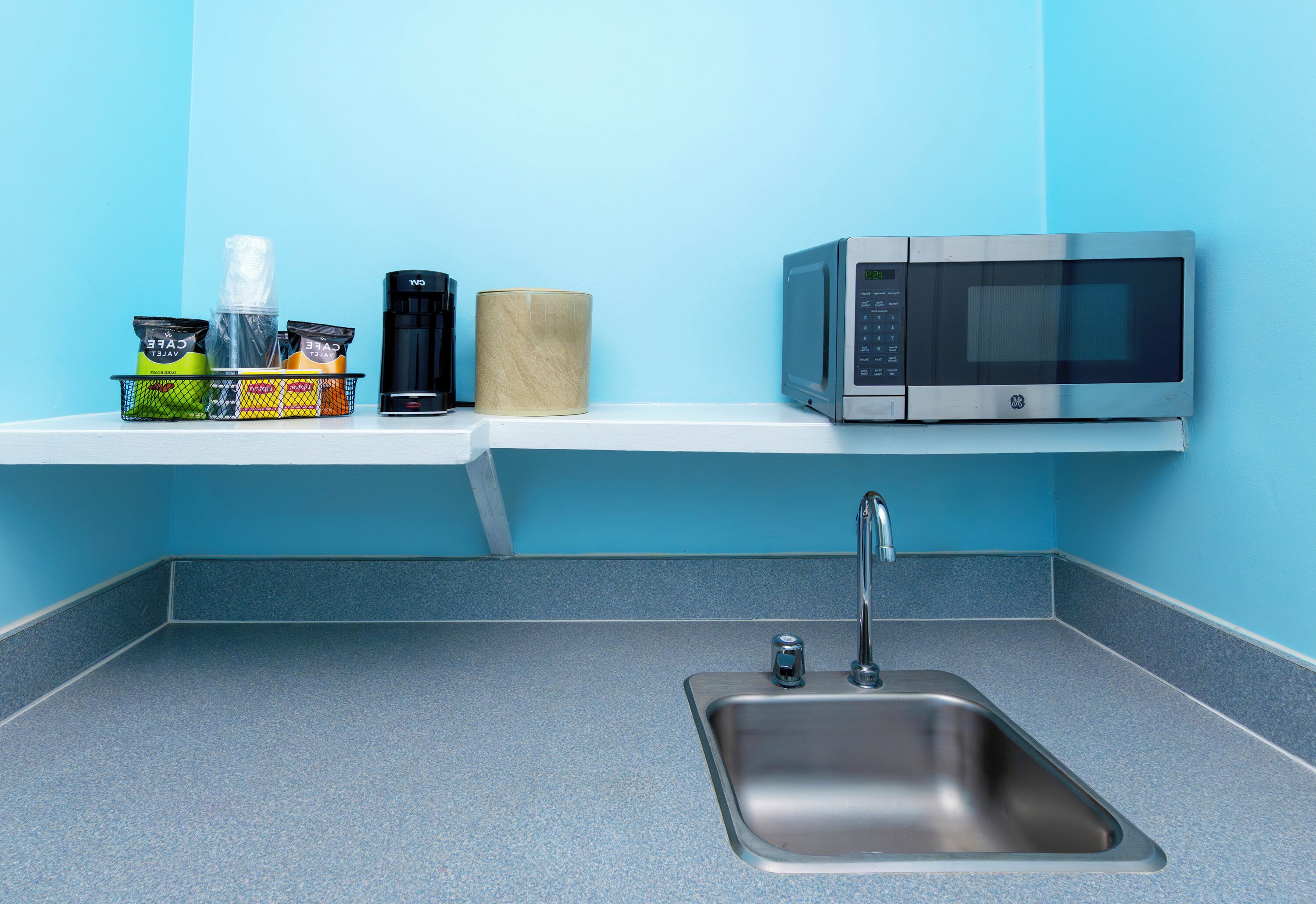 Una cocina con un lavamanos de acero inoxidable, un microondas y una repisa con alimentos.