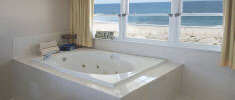 A bathroom with a large bathtub, a window with a beach view, and a towel rack.