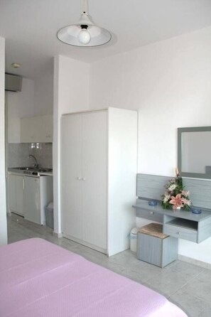 Un dormitorio moderno con una cama grande, una mesita de noche, un espejo y una pequeña cocina integrada al fondo.