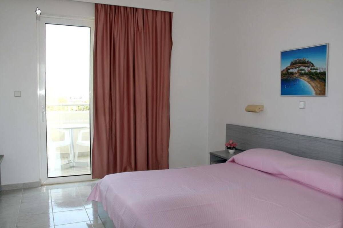 A hotel room with a bed, a nightstand, a painting, and a view of a balcony.