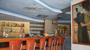 Zona de bar con taburetes de madera, un mural en el techo y estantes llenos de botellas de licor.
