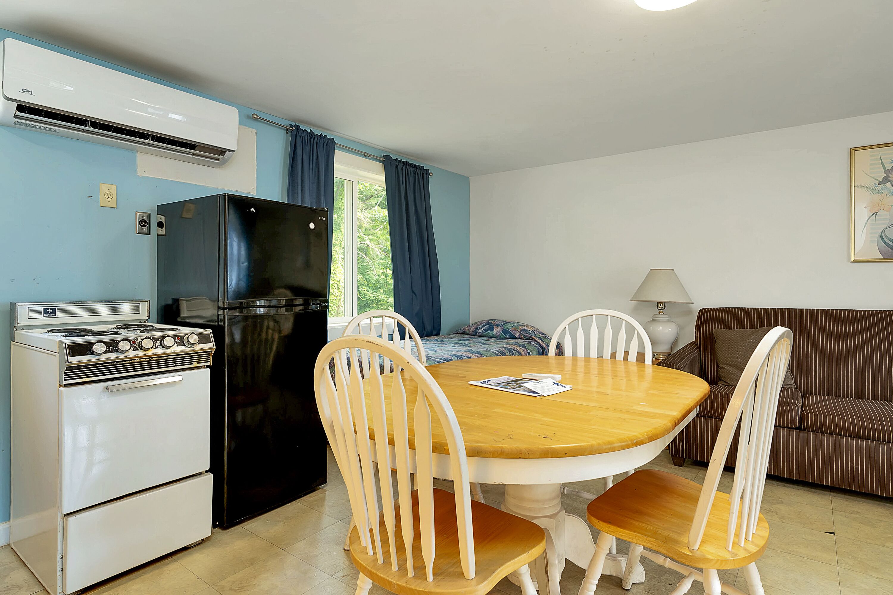 Una cocina compacta con estufa, refrigerador y mesa de comedor con sillas.