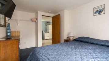 Une chambre à coucher comprenant un lit, une commode, un téléviseur et une porte donnant sur un coin cuisine.