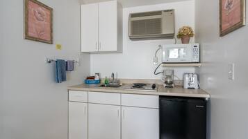 Una cocina compacta con armarios blancos, un lavavajillas negro, microondas, cafetera y un lavabo pequeño.