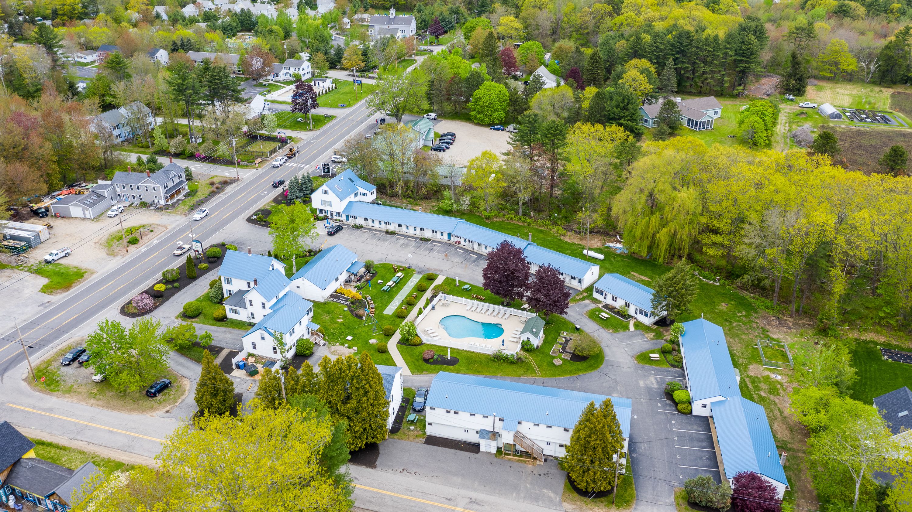 An aerial view of a resort with a swimming pool, multiple guest buildings, and a well-maintained landscape.