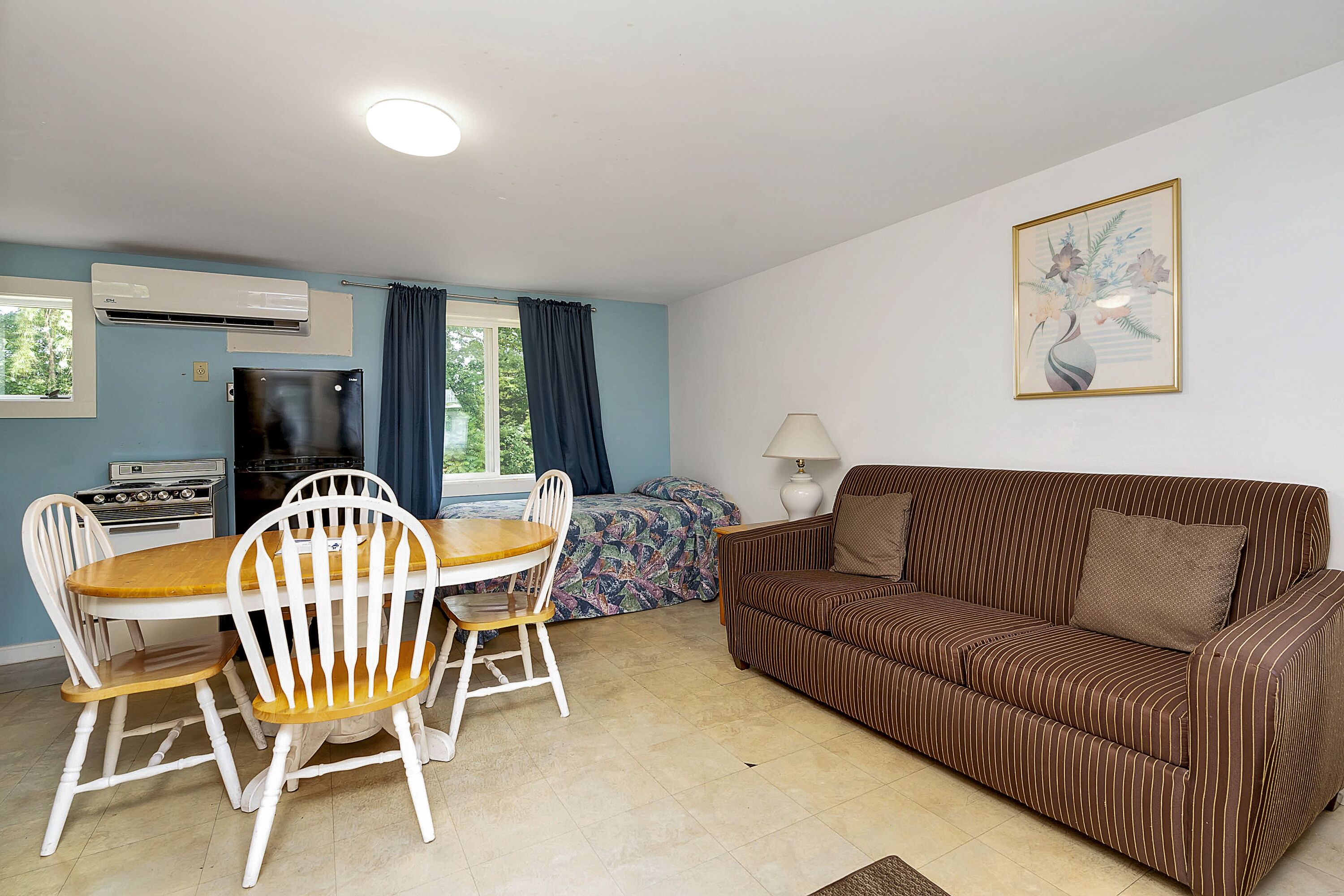 A living room with a striped sofa, a dining table with chairs, a TV, and a window with curtains.