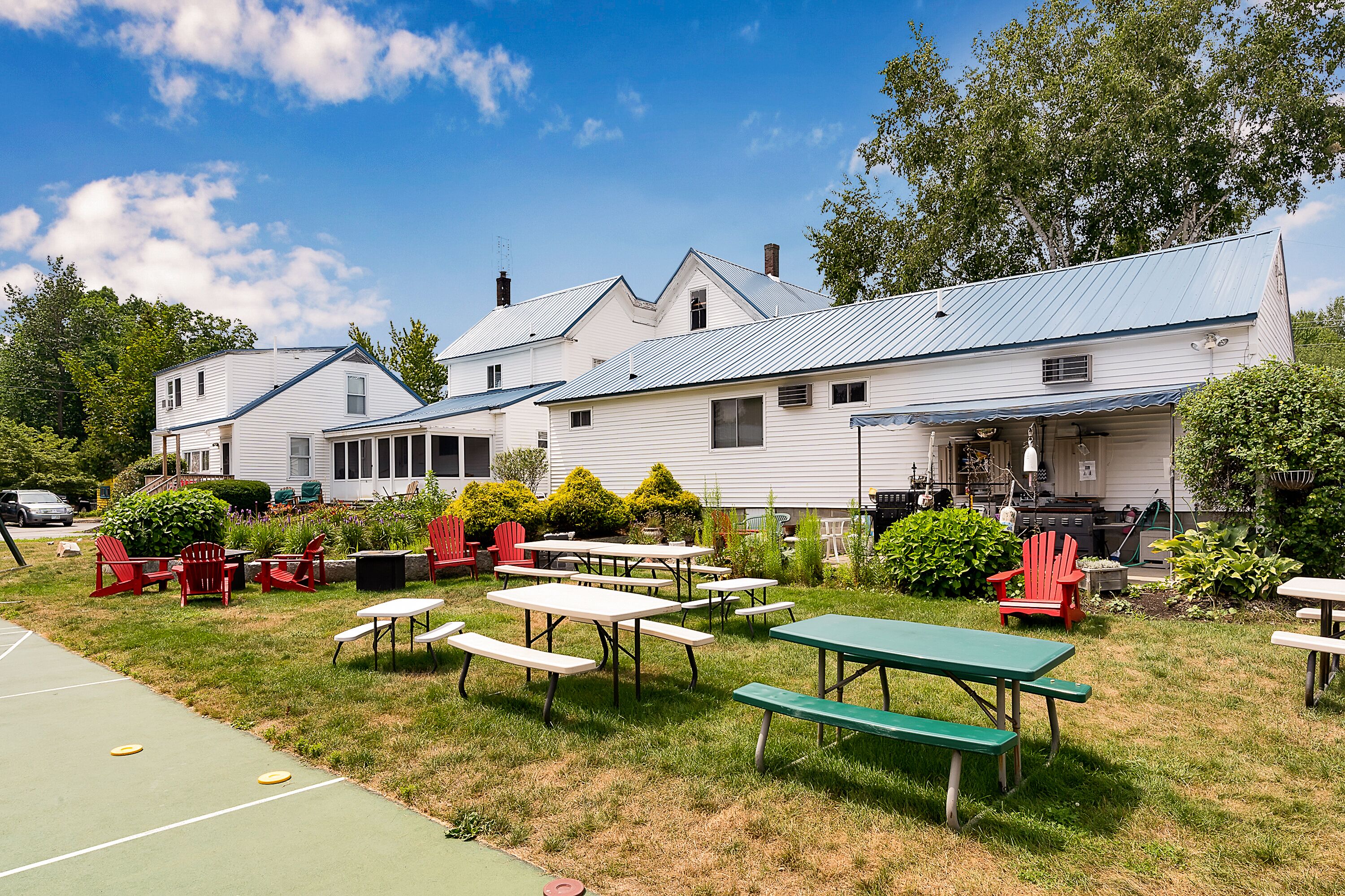 A row of white buildings with a patio area featuring picnic tables and red Adirondack chairs.
