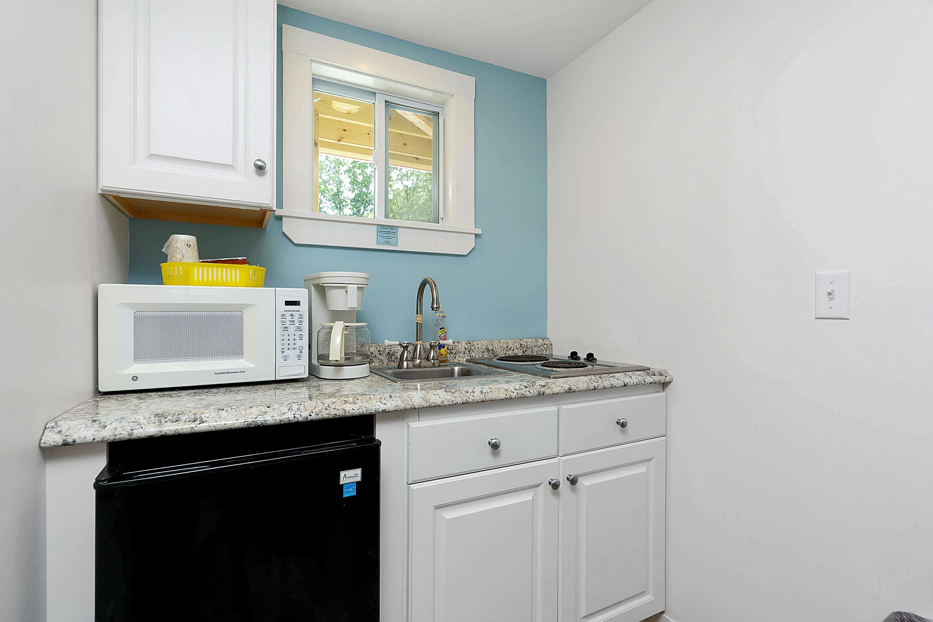 A compact kitchen with white cabinets, a microwave, a coffee maker, and a dishwasher.
