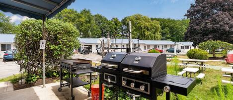 A covered outdoor area with a barbecue grill, picnic tables, and a small trash bin.
