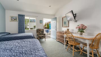A bedroom with two beds, a desk with chairs, a dresser, and a TV.