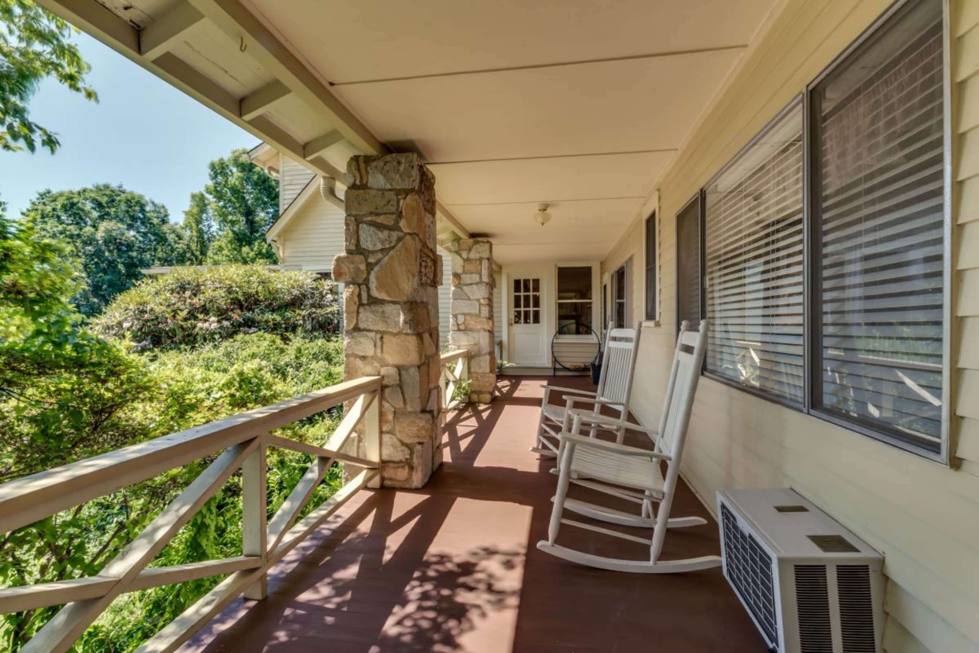 A covered porch with stone pillars, a wooden railing, and a white air conditioning unit.